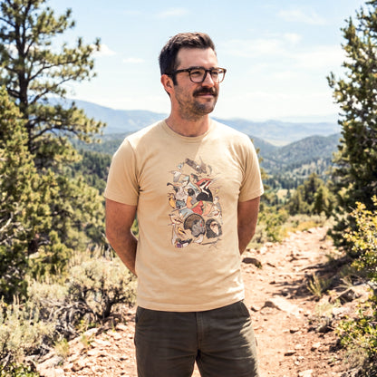 Man standing in a mountainous landscape, wearing a beige t-shirt with a graphic design of North American bird species.